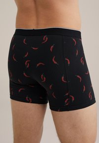 Melnu zīmuļu šorti ar atkārtotu sarkano un zaļo čili piparu rakstu. Elastīga jostasvieta, cieši pieguļošs piegriezums, līdz vidus ceļgaliem.