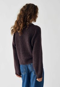 Pulover lână de culoare mov închis, pufos, cu decolteu rotund și mâneci lungi, purtat împreună cu blugi din denim albastru, cu talie înaltă.