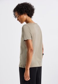 Khaki-värinen, lyhythihainen T-paita, jossa on pyöreä kaula-aukko. Pehmeä, sileä pinta, hieman rento malli ja minimaaliset saumat.