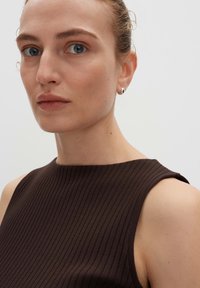 Brown ribbed sleeveless top with a high neckline. Smooth texture and fitted design, featuring subtle shoulder detailing and natural skin tones.