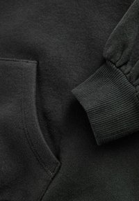 Felpa nera con cappuccio dotata di tasca a marsupio e polsini a costine. Il materiale ha una texture liscia con un interno morbido e spazzolato.
