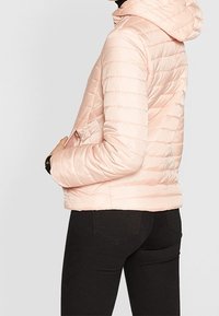 Jasnoróżowa kurtka puchowa z poziomym pikowaniem, kapturem, kieszeniami z przodu i elastycznymi mankietami. Gładki, błyszczący materiał.