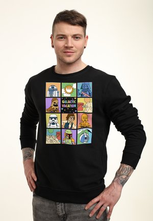 Man draagt een zwarte trui met kleurrijke stripachtige panelen van Star Wars-personages en de tekst "Galactic Vacation."