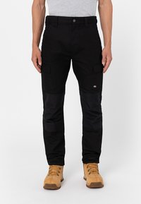 Black cargo pants with multiple pockets, contrasting fabric panels, and a fitted design. Paired with tan boots featuring lace-up detailing.