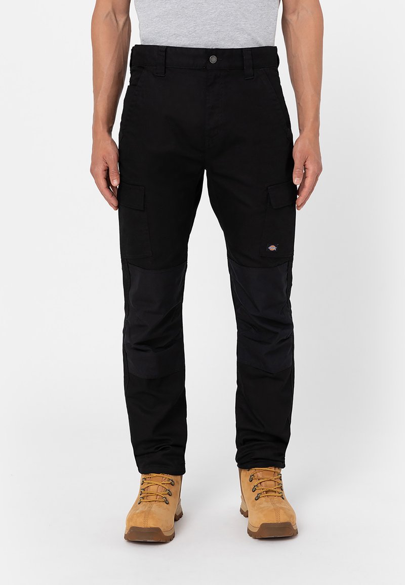Black cargo pants with multiple pockets, contrasting fabric panels, and a fitted design. Paired with tan boots featuring lace-up detailing.
