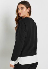 Mustat hupparit, joissa on pitkät hihat, pyöreä pääntie ja kontrastivärinen valkoinen kaulus kerroksittain alla. Pehmeä materiaali ja rento istuvuus.