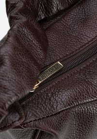 Borsa in pelle marrone con texture e chiusura a zip, con un'etichetta in metallo dorato che riporta la scritta "WITTCHEN". Dettagli del design stropicciati visibili.