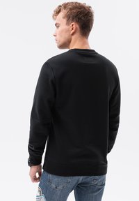 Schwarzer Sweatshirt mit Rundhalsausschnitt, gerippten Bündchen und Saum. Glatte Textur, minimalistisches Design. Getragen mit hellblauen Jeans.