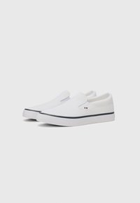 White slip-on shoes with a textured canvas upper, elastic side panels, and a white rubber sole featuring a navy blue stripe.