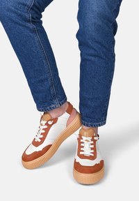 Sneaker in suede bianco e marrone con suola in tan texturizzata, caratterizzati da un design a scallop, chiusura con lacci e lati con ritagli.