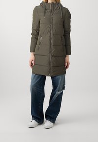 Olivgrön vadderad jacka med huva, främre dragkedjestängning och två sidofickor. Jackan har ett quiltat mönster och långa ärmar.