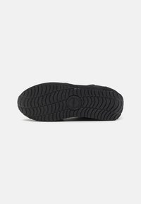 Svart sneakersåle med et multidireksjonelt mønster, teksturert gummimateriale, og en rund logo i midten av buen.