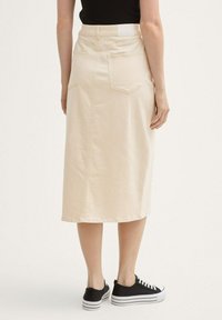 Cremfarbene Denim-Midirock mit aufgesetzten Rückentaschen, geradem Schnitt und subtiler Textur. Kombiniert mit schwarzen Schnürsneakern.