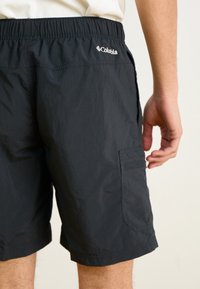 Melnās Columbia šortos ar elastīgu jostu, sānu kabatu un nelielu spīdumu. Materiāls izskatās viegls un elpojošs.