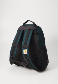 Rygsæk med et teal og sort design, der har polstrede skulderremme, justerbare spænder og en mesh sidelomme. Carhartt-logoet vises.