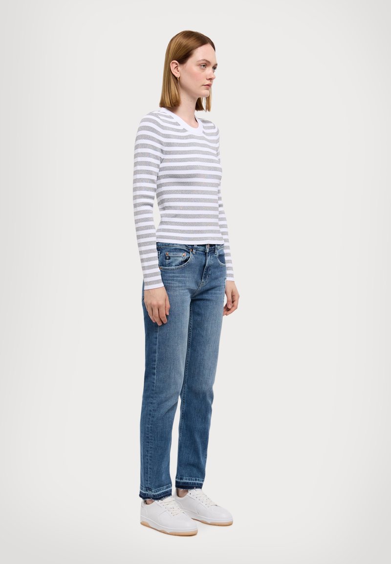 Camicia a maniche lunghe a righe bianca e grigia, abbinata a jeans blu. L'outfit è completato da sneakers bianche con suola in gomma.