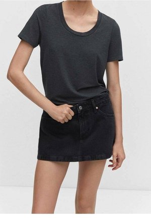 Femme portant un t-shirt gris foncé à manches courtes rentré dans une mini-jupe en jean noire taille haute avec boutons et poches devant.