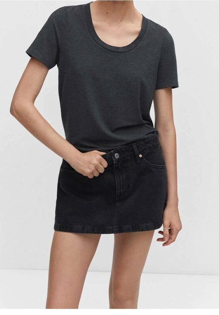 Femme portant un t-shirt gris foncé à manches courtes rentré dans une mini-jupe en jean noire taille haute avec boutons et poches devant.