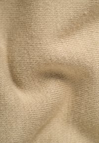 Beiger Strickstoff mit weicher Textur, der eng verwobene Fäden und eine leichte Dehnbarkeit in einem glatten, welligen Muster aufweist.