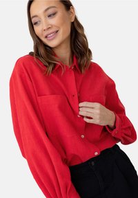 Czerwona, długosleeve koszula z miękkiego materiału, z dwiema kieszeniami na piersiach, zapięciem na guziki i luźnym krojem, w zestawie z czarnymi spodniami.