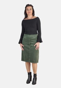 Top negro de manga larga con escote barco, combinado con una falda midi de pana verde con botones frontales y bolsillos. Botines negros.