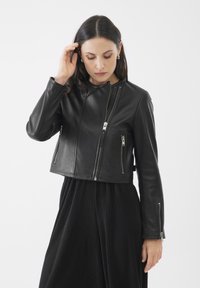 Giacca cropped in pelle nera con cerniere argentate, dotata di un collo alto e di molteplici tasche con cerniera nella parte anteriore e laterale.