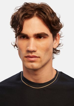 Gold-toned metal chain necklace worn over a dark crew-neck shirt. The necklace features a smooth, curved design with a delicate texture.
