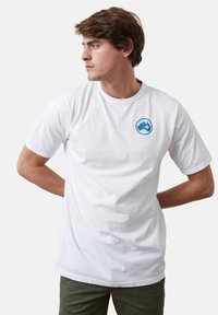 Camiseta de algodón blanca con un logo circular azul en el pecho. Manga corta y un clásico escote redondo. Textura suave y ajuste regular.