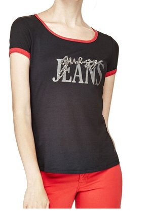 Person trägt ein schwarzes T-Shirt mit rotem Rand und "Guess Jeans" Text, kombiniert mit leuchtend roten Hosen, gezeigt vom Hals bis zur Hüfte.