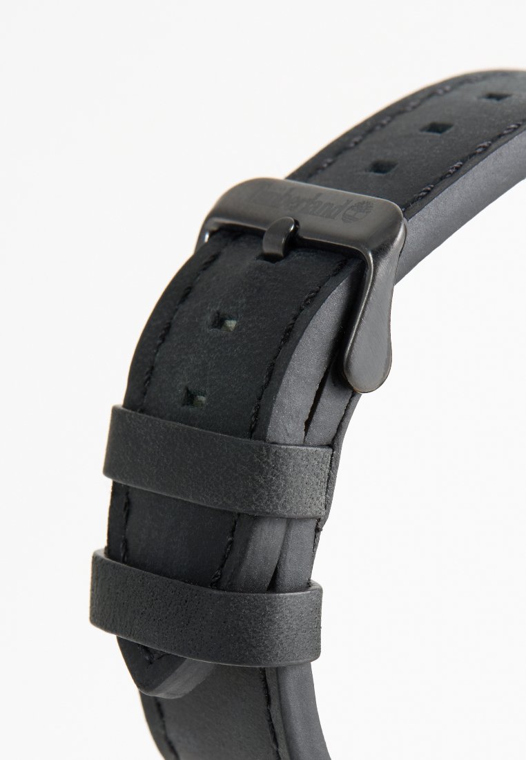 Correa de reloj de cuero negro con perforaciones, hebilla ajustable y dos bucles de retención. Acabado texturizado con un reverso suave.