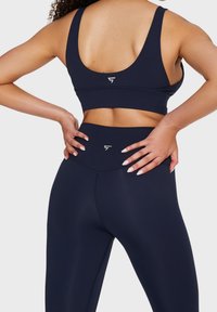 Marinblå sport-bh och högmidjade leggings tillverkade av ett mjukt, elastiskt material. Har minimal branding och en åtsittande passform för stöd.