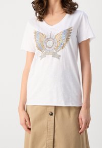 Bílý krátký rukáv tričko s V-výstřihem; má barevnou grafiku s křídly v zlaté, modré a stříbrné barvě s detaily stuhy.