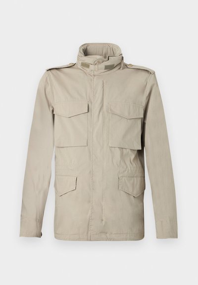 Veste militaire beige avec un col haut, quatre poches avant et des épaulettes. Le tissu est lisse avec une texture légère.