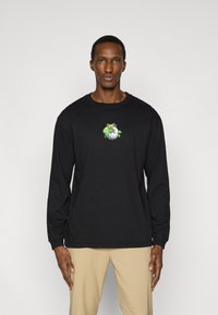 Μαύρο μακρυμάνικο  μπλουζάκι με στρογγυλή λαιμόκοψη που διαθέτει πολύχρωμο γραφικό ενός πράσινου χαρακτήρα σε μπάλα του γκολφ. Απαλό βαμβακερό υλικό.