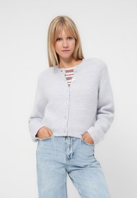 Ljusgrått kort cardi med rund halsringning, mjuk textur och fem blå knappar, kombinerat med hög midja ljusblå jeans.