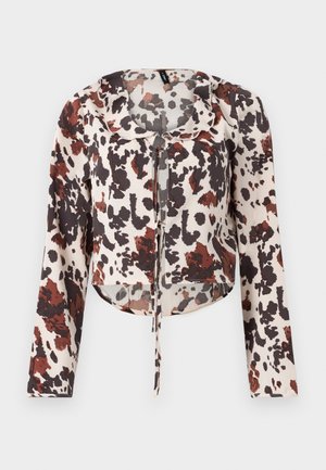 Blouse raccourcie avec cordon de serrage, présentant une base beige et un imprimé abstrait brun et rouge. Manches longues et tissu doux et texturé.