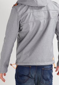 Grijze jas met capuchon, met oranje accenten en verstelbare trekkoorden. Gladde stof met gestikte details op de achterkant.