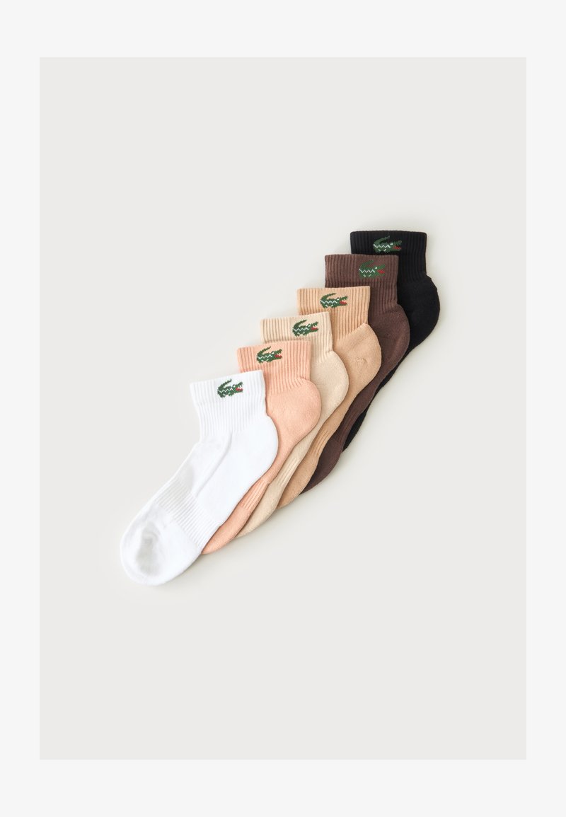 Sept paires de chaussettes basses côtelées en blanc, pêche, beige, marron clair, marron foncé et noir avec un logo crocodile vert.