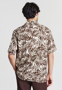 Camicia a maniche corte in marrone e crema con motivo a foglie. Presenta un colletto e una vestibilità comoda, realizzata in tessuto leggero.