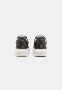 Mustad sneakers tekstuuriga viimistlusega, millel on korduv pruun muster. Valged taldad ja kontrastsed tumedad aktsendid lõpetavad disaini.