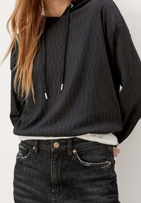 Sudadera negra texturizada con cordón y extremos en plateado. Combinada con unos jeans negros de cintura alta con detalles desgastados.
