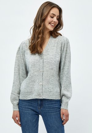 Šedý pletený svetr s výstřihem do V, zapínáním na knoflíky a dvěma předními kapsami. Má žebrované manžety a volný střih. Měkká textura.