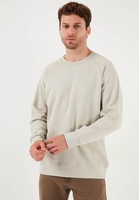 Felpa grigia chiara con collo a giro e maniche raglan. Realizzata in tessuto morbido, presenta un piccolo logo sul petto.