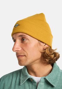 Berretto a coste giallo con una toppa ricamata a forma di diamante. La texture morbida completa il design aderente.