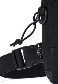 Dettaglio di una borsa nera in nylon che mostra una robusta tracolla regolabile, una fibbia in plastica e un'asola con un nodo per fissare accessori.