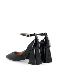 Black patent leather block heel shoes with an ankle strap, pointed toe, and smooth texture. Features a distinct geometric heel design.