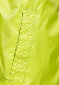 Un tissu jaune fluorescent avec une texture lisse présente une patch rectangulaire et des coutures contrastantes, mettant en valeur un élément de design durable.