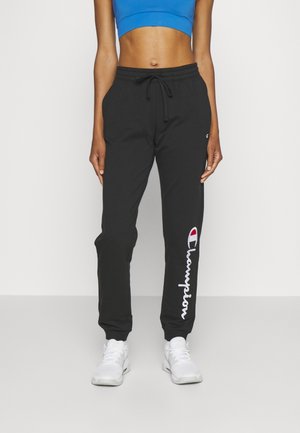 Black joggers with elastic waistband and drawstring. Features white "Champion" logo along the leg. Paired with a blue crop top and white sneakers.