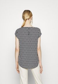 Blusa a maniche corte in bianco e nero con un collo rotondo e orlo curvo, caratterizzata da un design geometrico astratto.