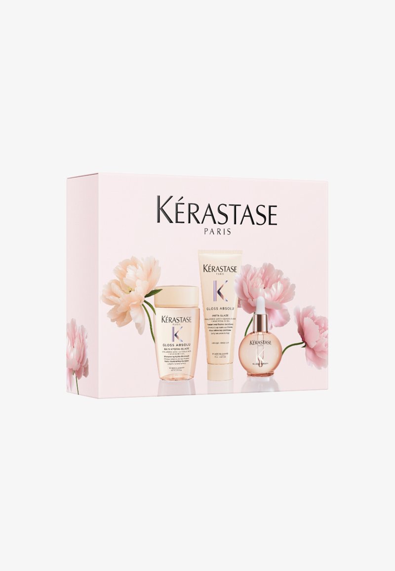 Set de soins capillaires Kérastase Paris Gloss Absolu avec des flacons de shampooing, de crème et de sérum sur une boîte rose décorée avec des fleurs rose pâle.